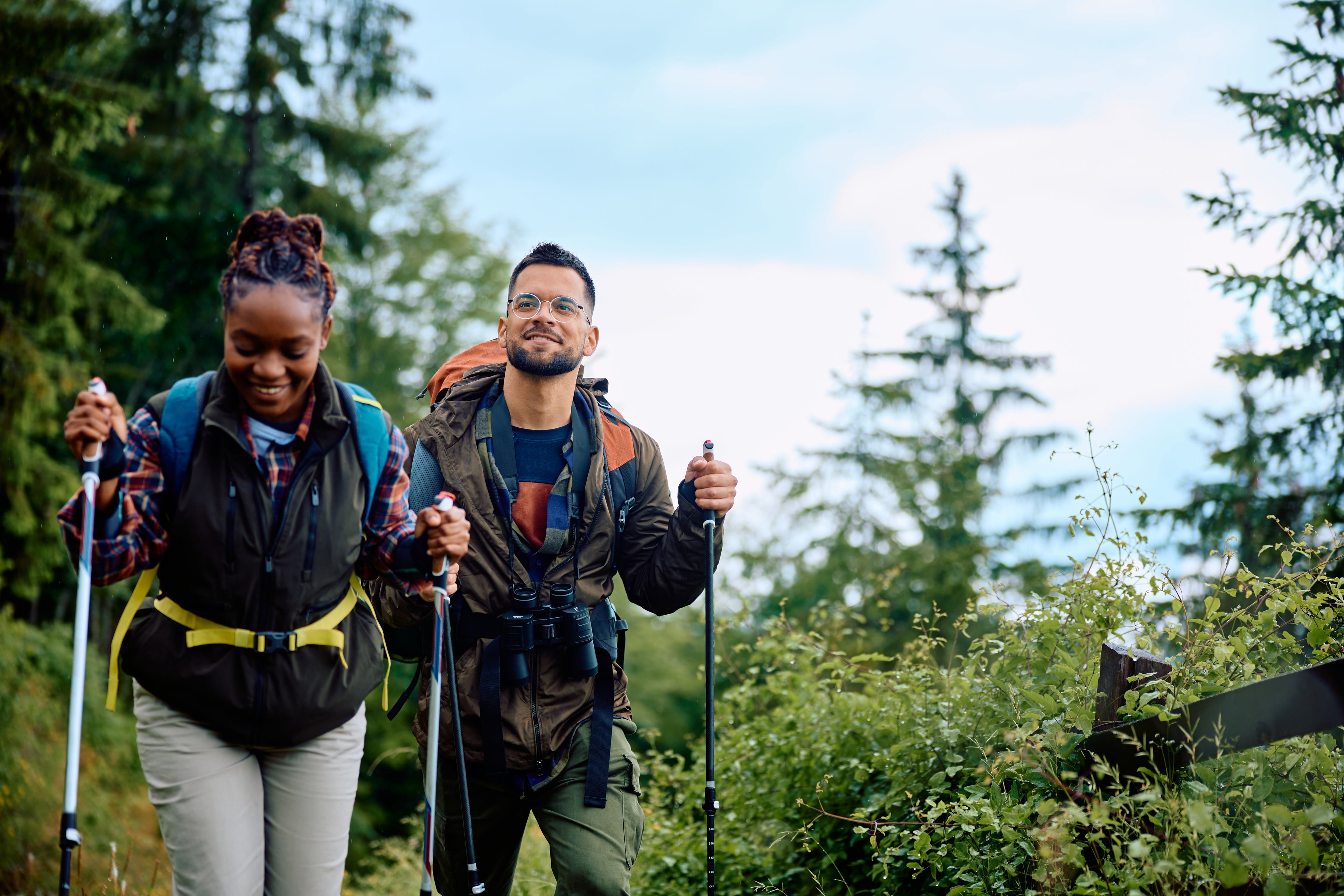 Two hikers walking through a forest with backpacks and hiking poles.